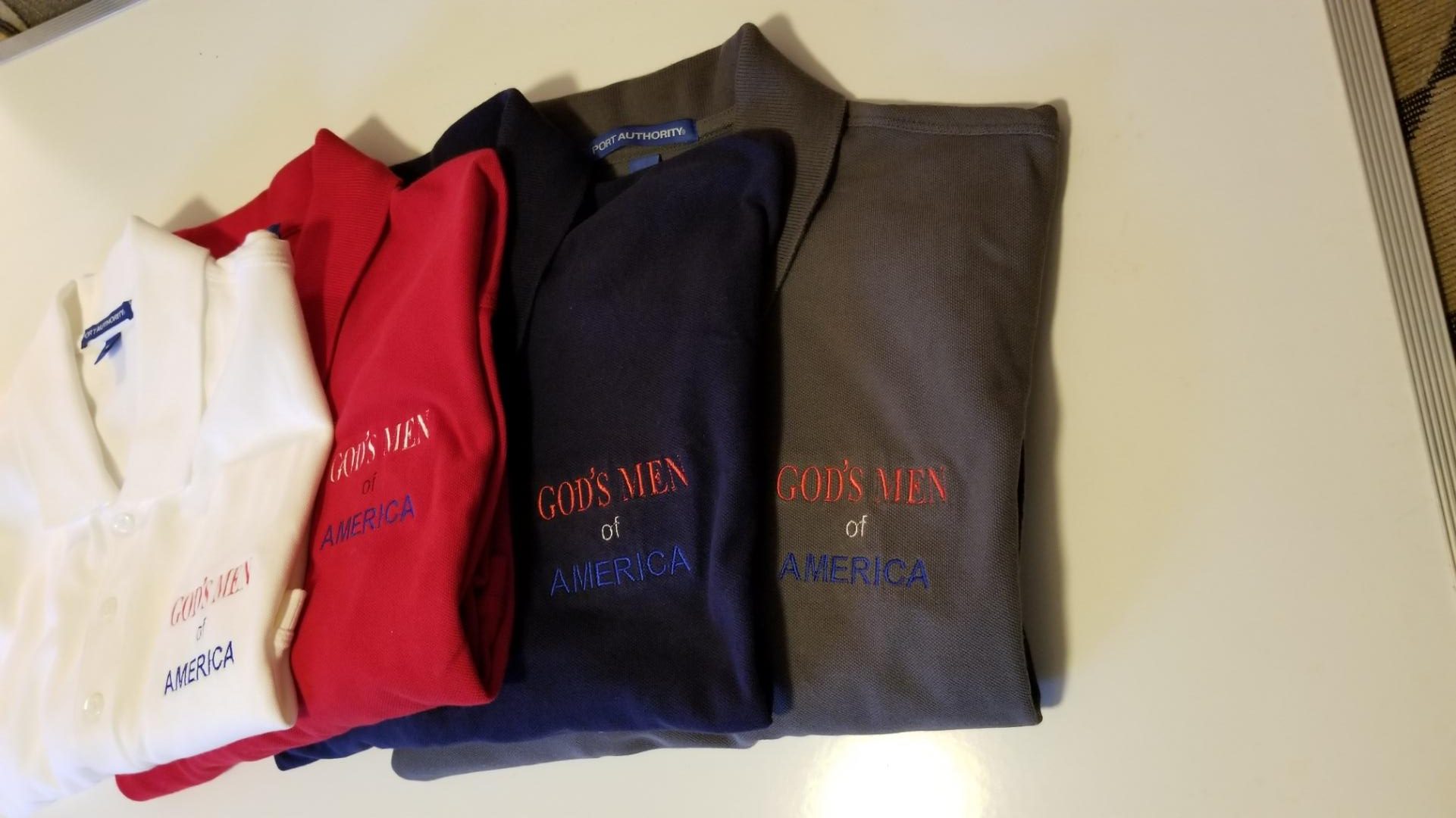 White, red, navy and gray God's Men of America polo shirts stacked together